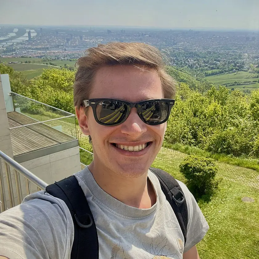 Peter, smiling in sunglasses, on a hilltop above a city.
